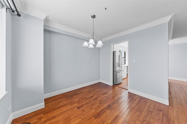 spare room featuring baseboards, wood-type flooring, an inviting chandelier, and crown molding