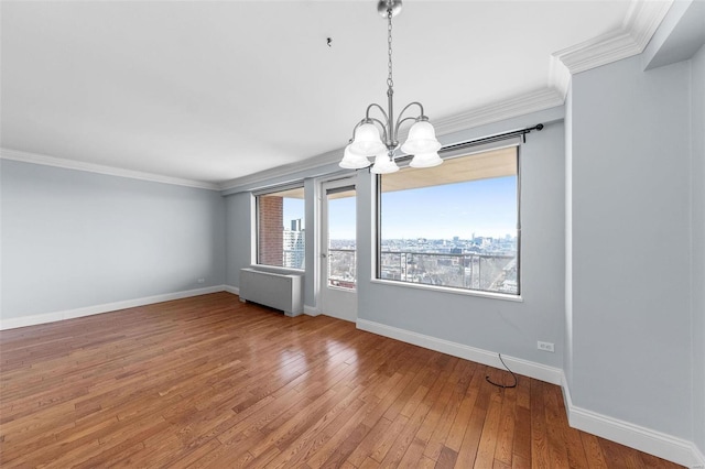 unfurnished room with light wood finished floors, crown molding, baseboards, a city view, and radiator heating unit