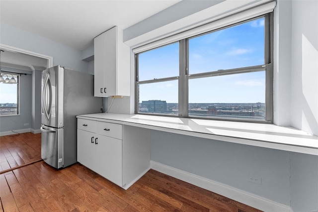 kitchen with dark wood finished floors, light countertops, built in desk, freestanding refrigerator, and white cabinets