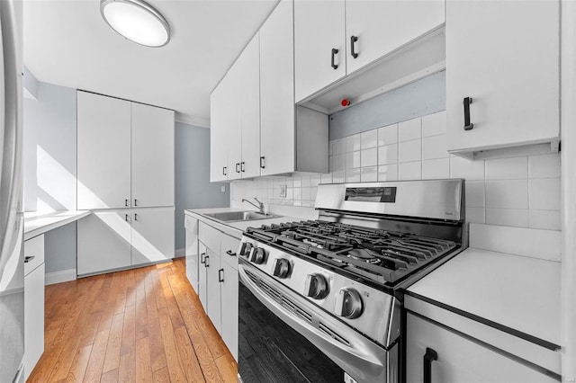 kitchen featuring light wood-style flooring, a sink, light countertops, decorative backsplash, and stainless steel range with gas stovetop