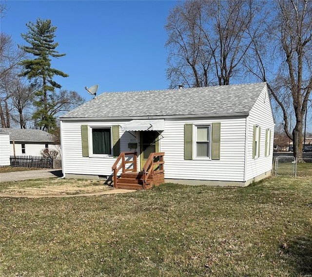 view of front facade with roof with shingles, a front yard, and fence