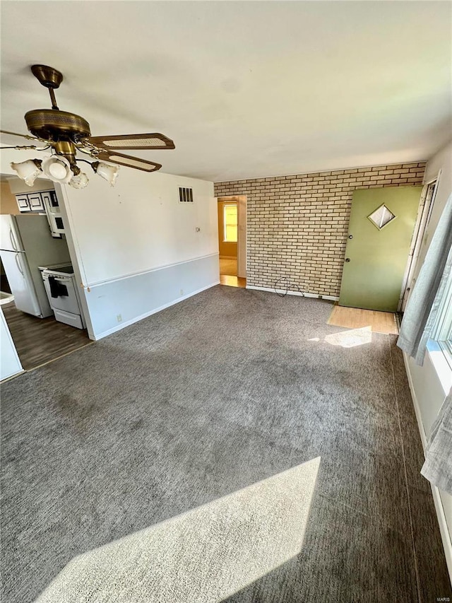 unfurnished living room with visible vents, carpet, brick wall, and a ceiling fan