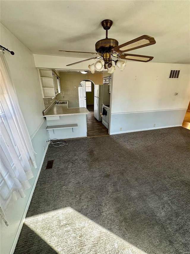 kitchen featuring white appliances, a ceiling fan, visible vents, arched walkways, and dark colored carpet