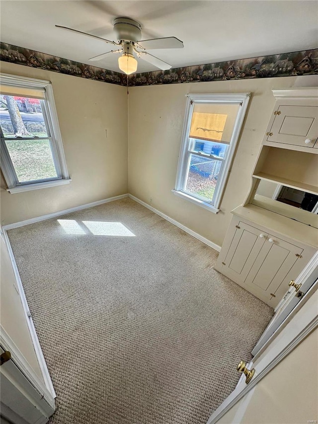 carpeted spare room with a wealth of natural light, baseboards, and ceiling fan