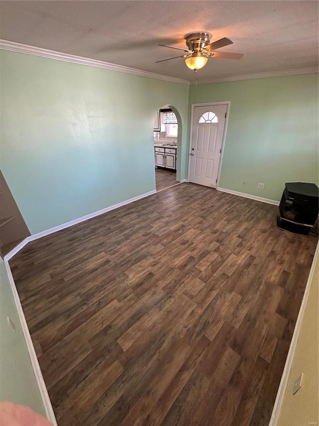 entrance foyer featuring dark wood-type flooring, a ceiling fan, arched walkways, crown molding, and baseboards