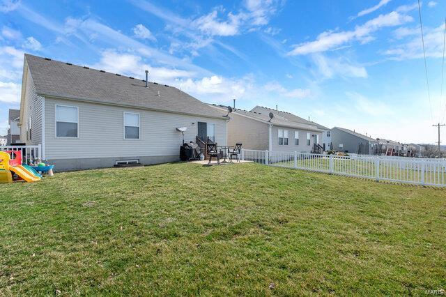 rear view of house with a yard, a fenced backyard, and a playground