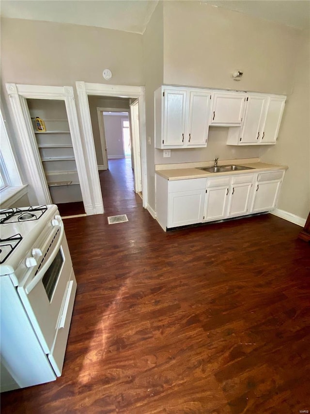 kitchen featuring dark wood-type flooring, light countertops, white range with gas stovetop, white cabinetry, and a sink