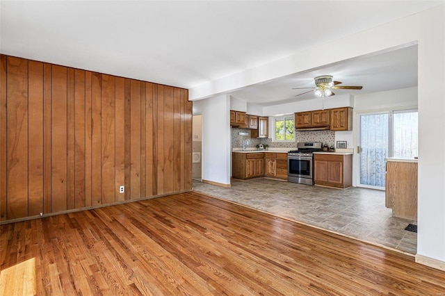 kitchen featuring brown cabinetry, under cabinet range hood, wood walls, light countertops, and stainless steel gas stove