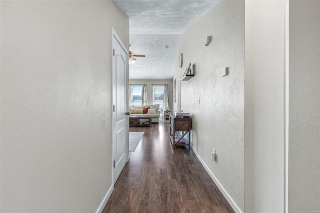 corridor featuring baseboards, wood finished floors, and a textured wall