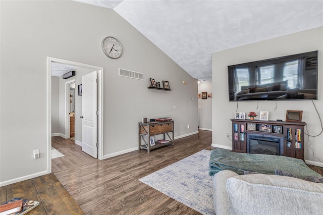 living room with a glass covered fireplace, visible vents, baseboards, and wood finished floors