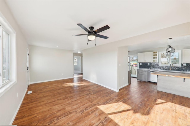 unfurnished living room with ceiling fan, baseboards, wood finished floors, and a sink