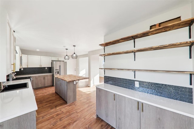 kitchen featuring light wood-type flooring, stainless steel refrigerator with ice dispenser, a sink, open shelves, and tasteful backsplash