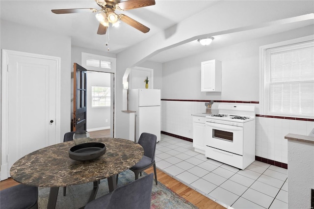 kitchen featuring white appliances, a wainscoted wall, arched walkways, white cabinets, and tile walls