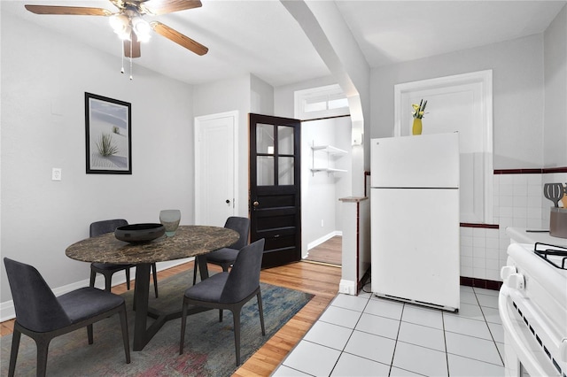 dining room with a ceiling fan, arched walkways, light wood finished floors, and baseboards