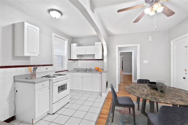 kitchen with a sink, white gas range oven, arched walkways, white cabinets, and light wood finished floors