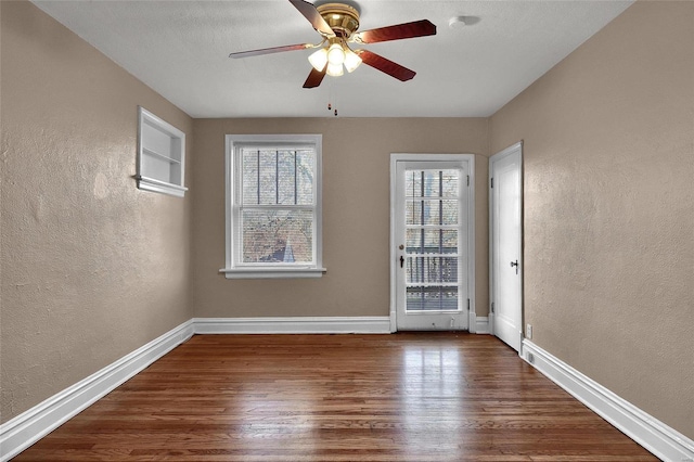 unfurnished room with baseboards, plenty of natural light, wood finished floors, and a textured wall