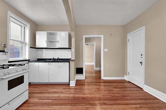 kitchen featuring baseboards, light wood-type flooring, decorative backsplash, dark countertops, and white gas range