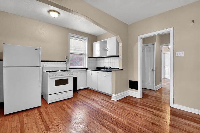 kitchen with white appliances, arched walkways, white cabinets, and light wood finished floors