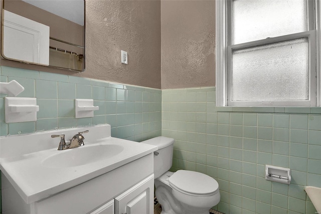 bathroom featuring toilet, tile walls, vanity, and a textured wall