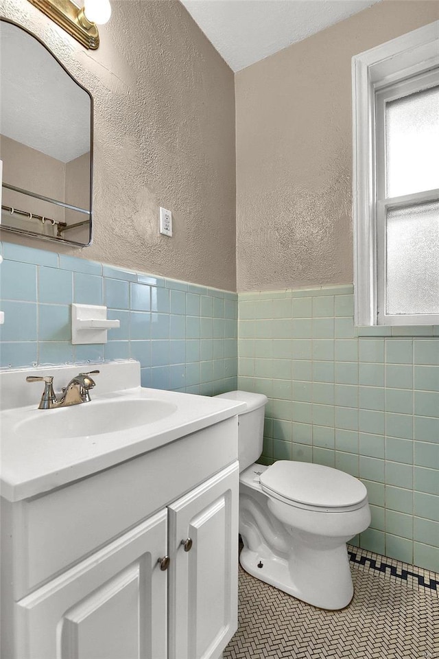 half bath featuring toilet, tile walls, tile patterned flooring, and a textured wall