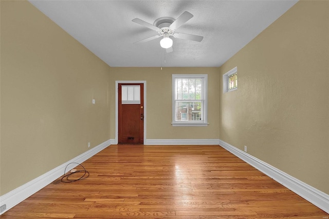 interior space with a ceiling fan, baseboards, light wood finished floors, and a textured ceiling