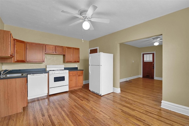 kitchen featuring dark countertops, white appliances, light wood-style floors, and a sink