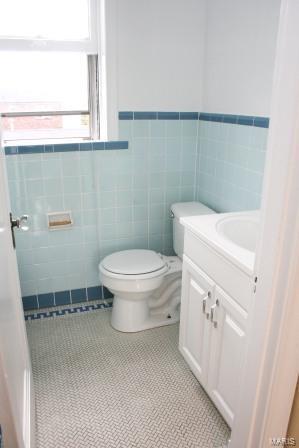 bathroom featuring a wainscoted wall, toilet, tile walls, tile patterned flooring, and vanity