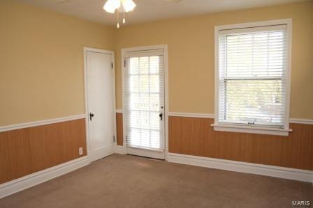 entryway with wooden walls, carpet, ceiling fan, and wainscoting