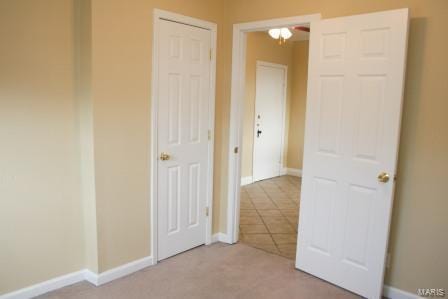 unfurnished bedroom featuring light tile patterned floors, baseboards, and light colored carpet