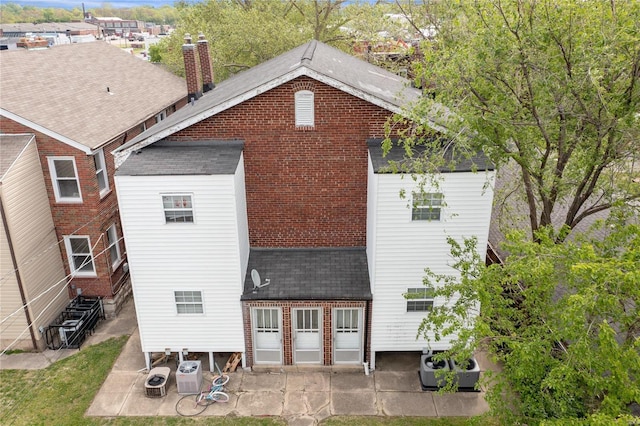 back of house with ac unit, entry steps, roof with shingles, a chimney, and a patio area