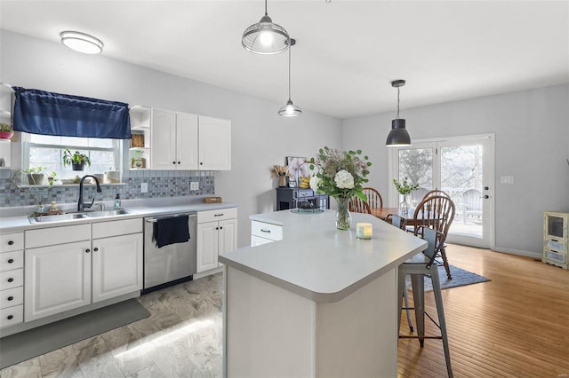 kitchen featuring a kitchen island, dishwasher, light countertops, decorative backsplash, and a sink