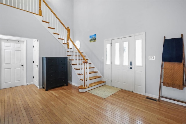 foyer entrance with visible vents, baseboards, stairway, a towering ceiling, and wood-type flooring