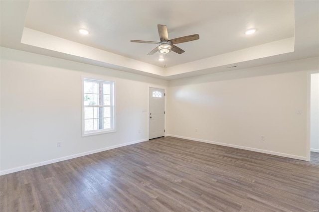 interior space with baseboards, a raised ceiling, and wood finished floors