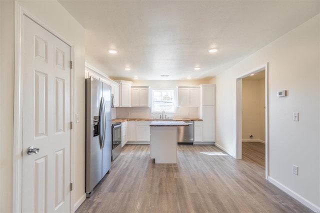 kitchen with a sink, a kitchen island, white cabinetry, stainless steel appliances, and light wood finished floors