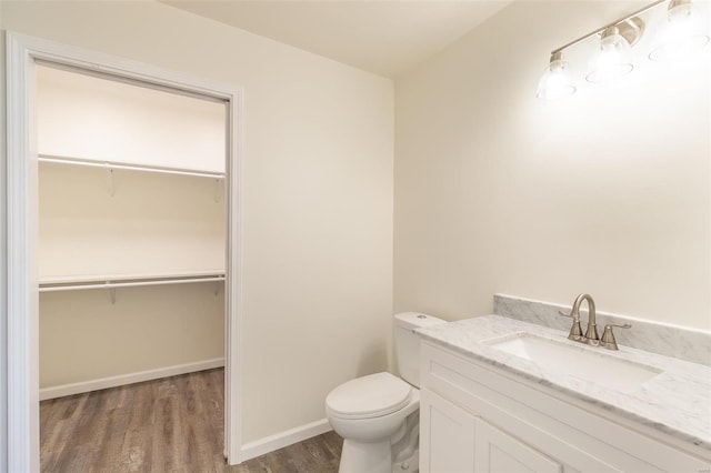 bathroom with vanity, toilet, wood finished floors, and a spacious closet