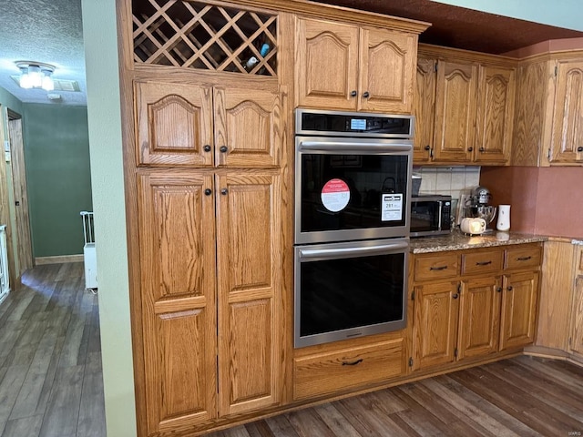 kitchen featuring light stone counters, stainless steel appliances, decorative backsplash, and dark wood-style flooring