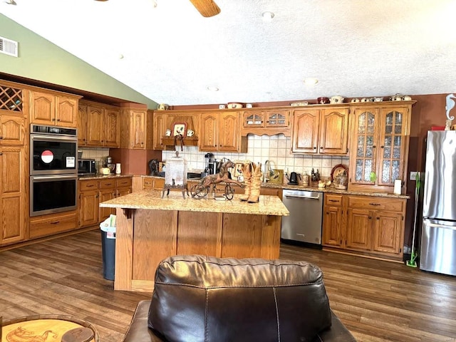 kitchen with vaulted ceiling, dark wood-type flooring, appliances with stainless steel finishes, and brown cabinets