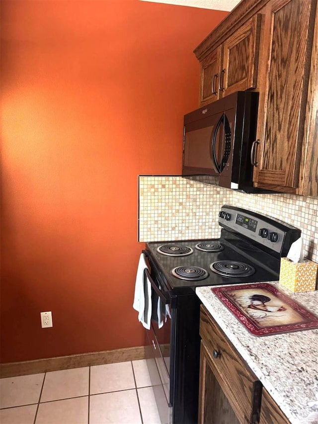 kitchen with stainless steel range with electric stovetop, backsplash, light tile patterned flooring, black microwave, and baseboards