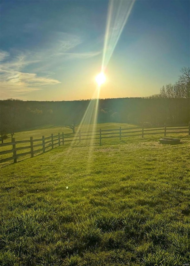 yard at dusk featuring a rural view and fence