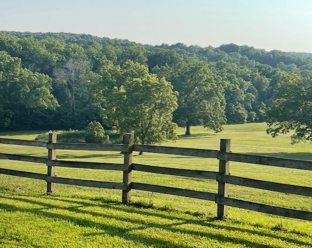 view of gate featuring a rural view, a wooded view, fence, and a lawn