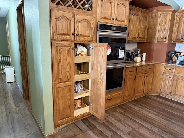 kitchen with double oven, light stone counters, and dark wood finished floors