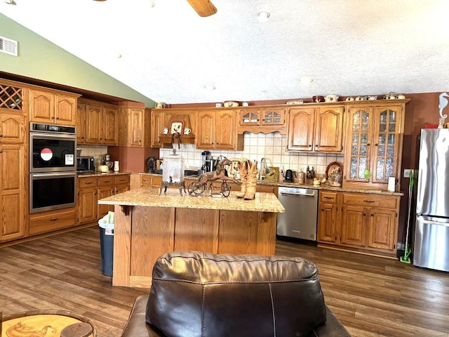 kitchen with brown cabinetry, dark wood-style flooring, appliances with stainless steel finishes, and lofted ceiling