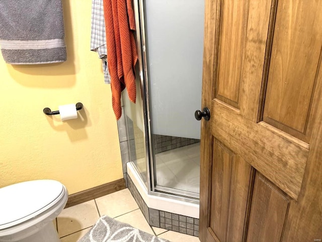 bathroom featuring toilet, a stall shower, tile patterned flooring, and baseboards