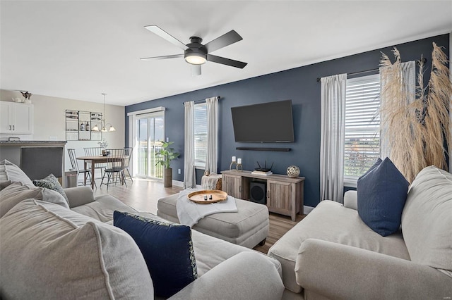 living room with ceiling fan with notable chandelier, baseboards, and wood finished floors