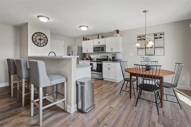 kitchen featuring baseboards, a breakfast bar, light wood-style flooring, stainless steel appliances, and white cabinets