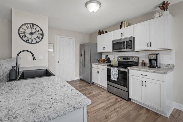 kitchen featuring light wood-style flooring, a sink, appliances with stainless steel finishes, white cabinets, and decorative backsplash