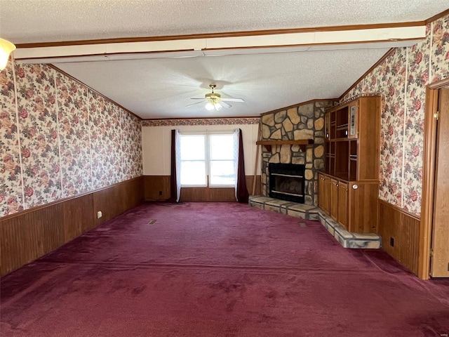 unfurnished living room with a stone fireplace, wainscoting, wallpapered walls, and a textured ceiling