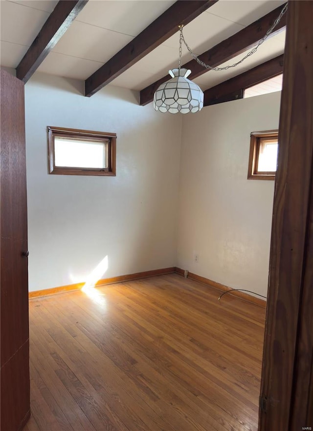 empty room featuring beam ceiling, wood finished floors, and baseboards