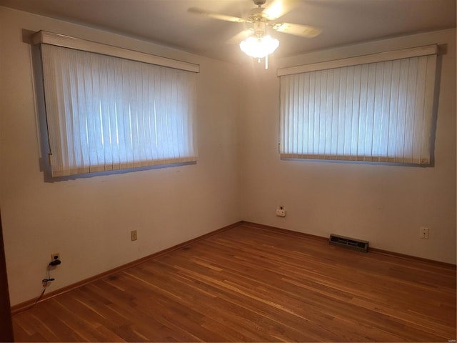 empty room with visible vents, a healthy amount of sunlight, wood finished floors, and a ceiling fan