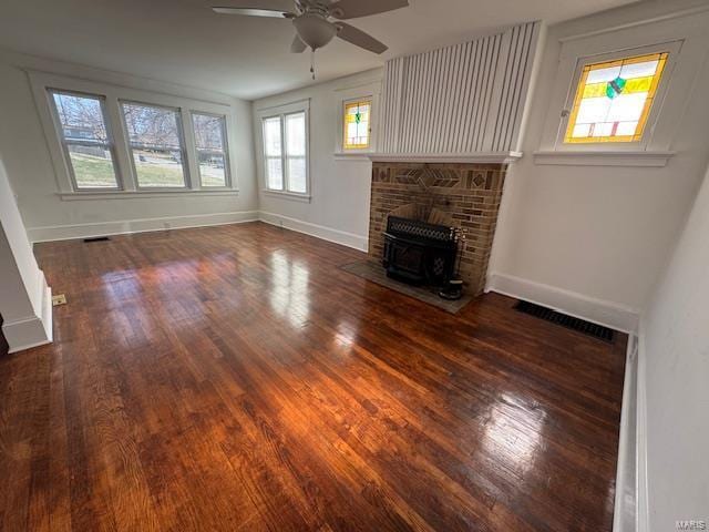 unfurnished living room with visible vents, baseboards, a wood stove, wood finished floors, and a ceiling fan